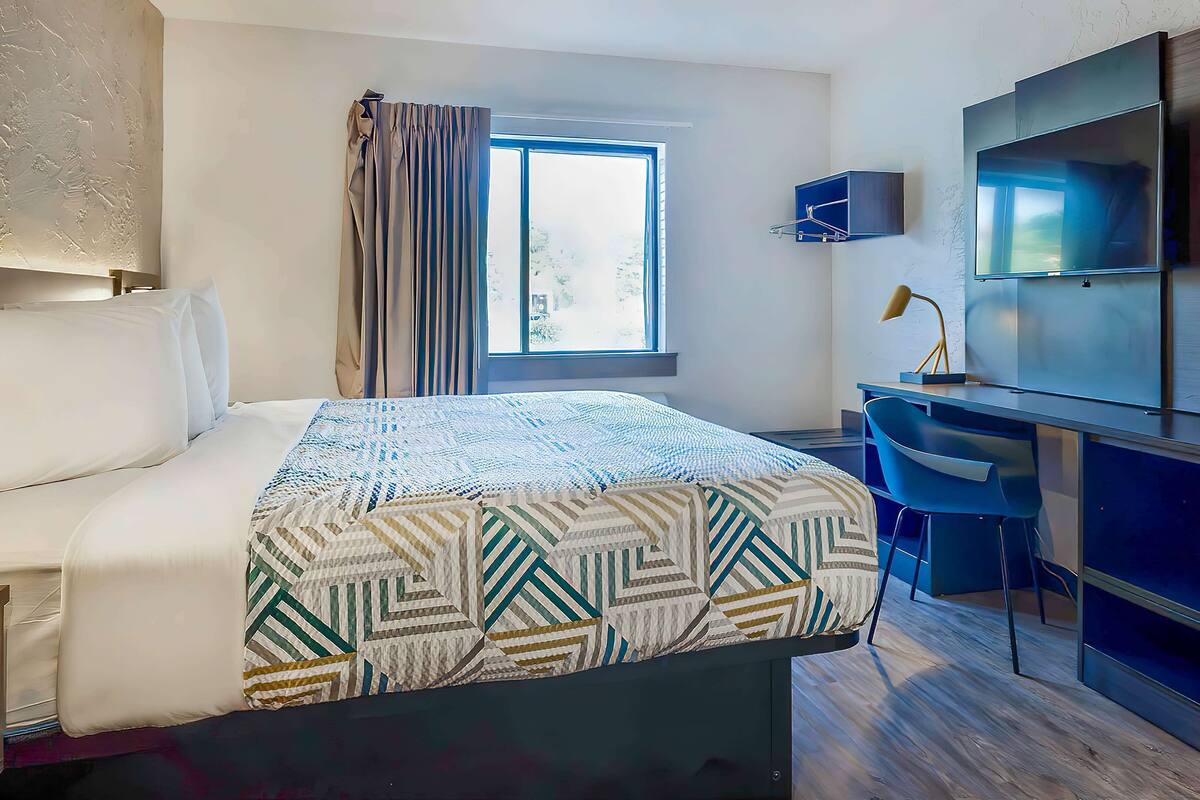 A hotel room with a bed, a desk, a chair, a TV, and a window with curtains.