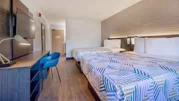 A hotel room with two beds, a desk with a chair, a TV, and a bathroom visible through an open door.