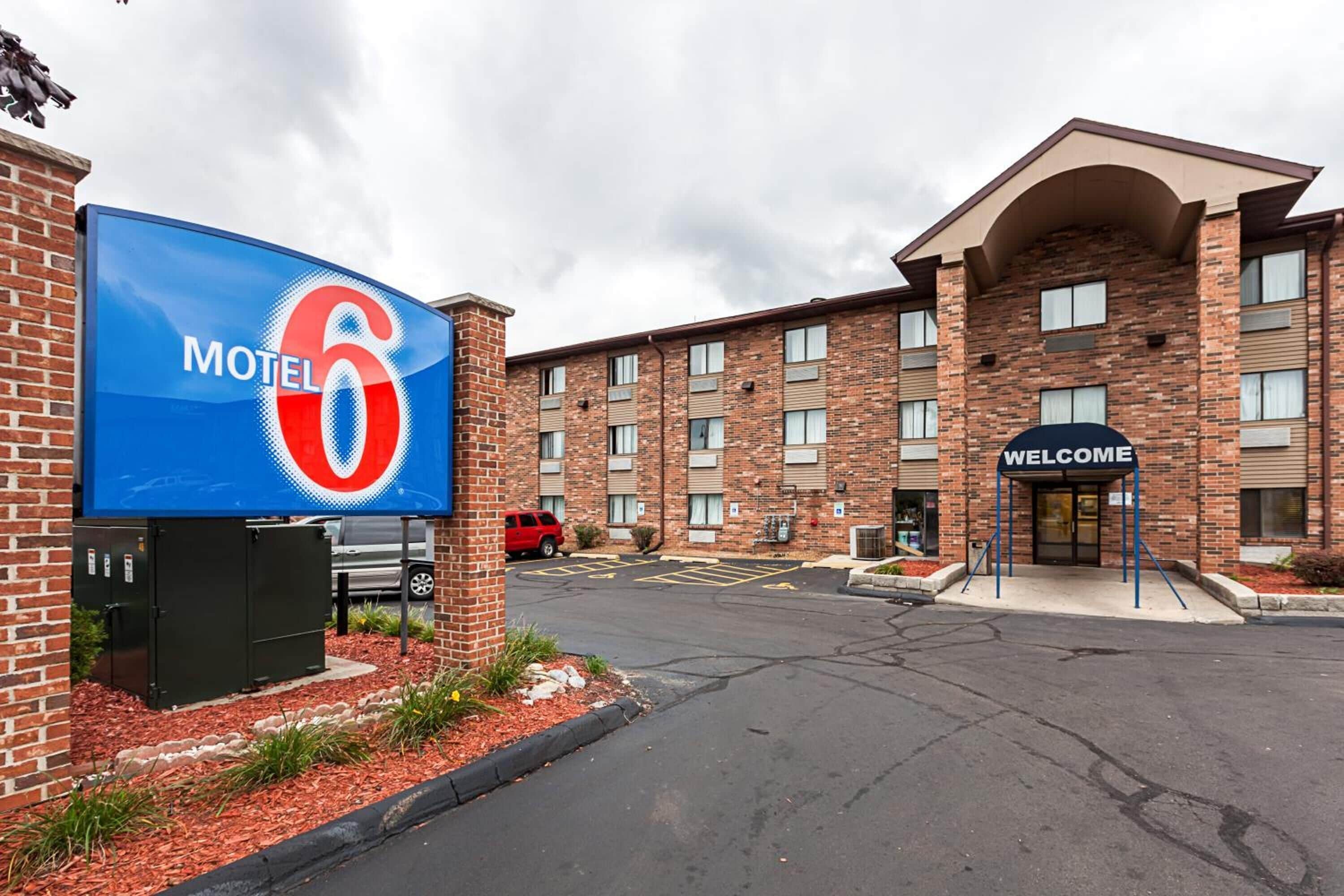 A brick building with a large blue sign reading "Motel 6" and a "Welcome" sign at the entrance.