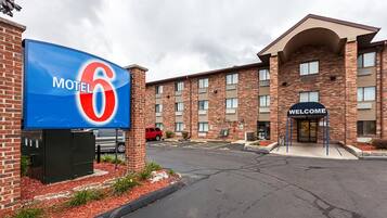 A brick building with a large blue sign reading "Motel 6" and a "Welcome" sign at the entrance.