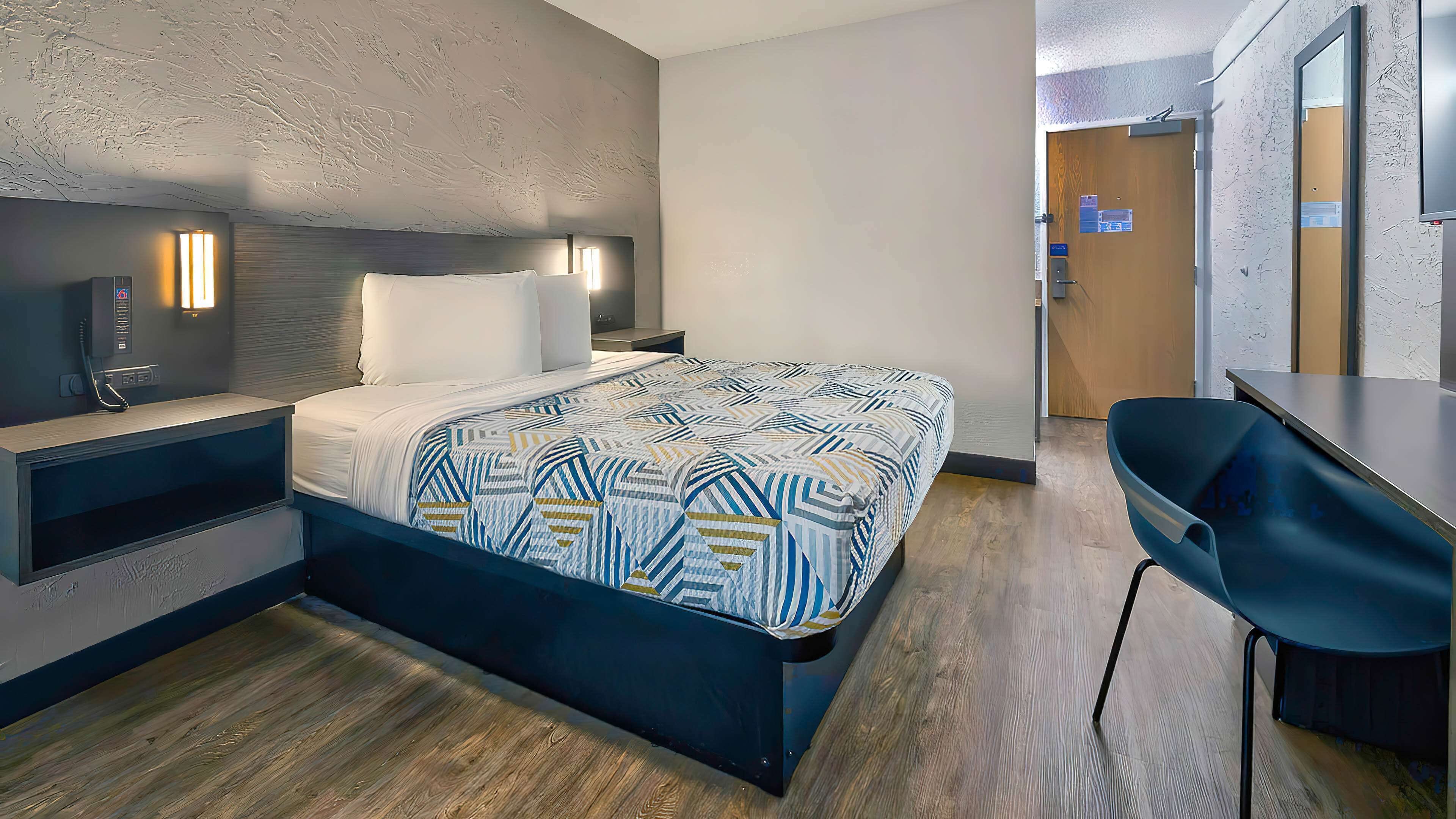 Una habitación de hotel moderna con cama, mesita de noche y escritorio con silla.
