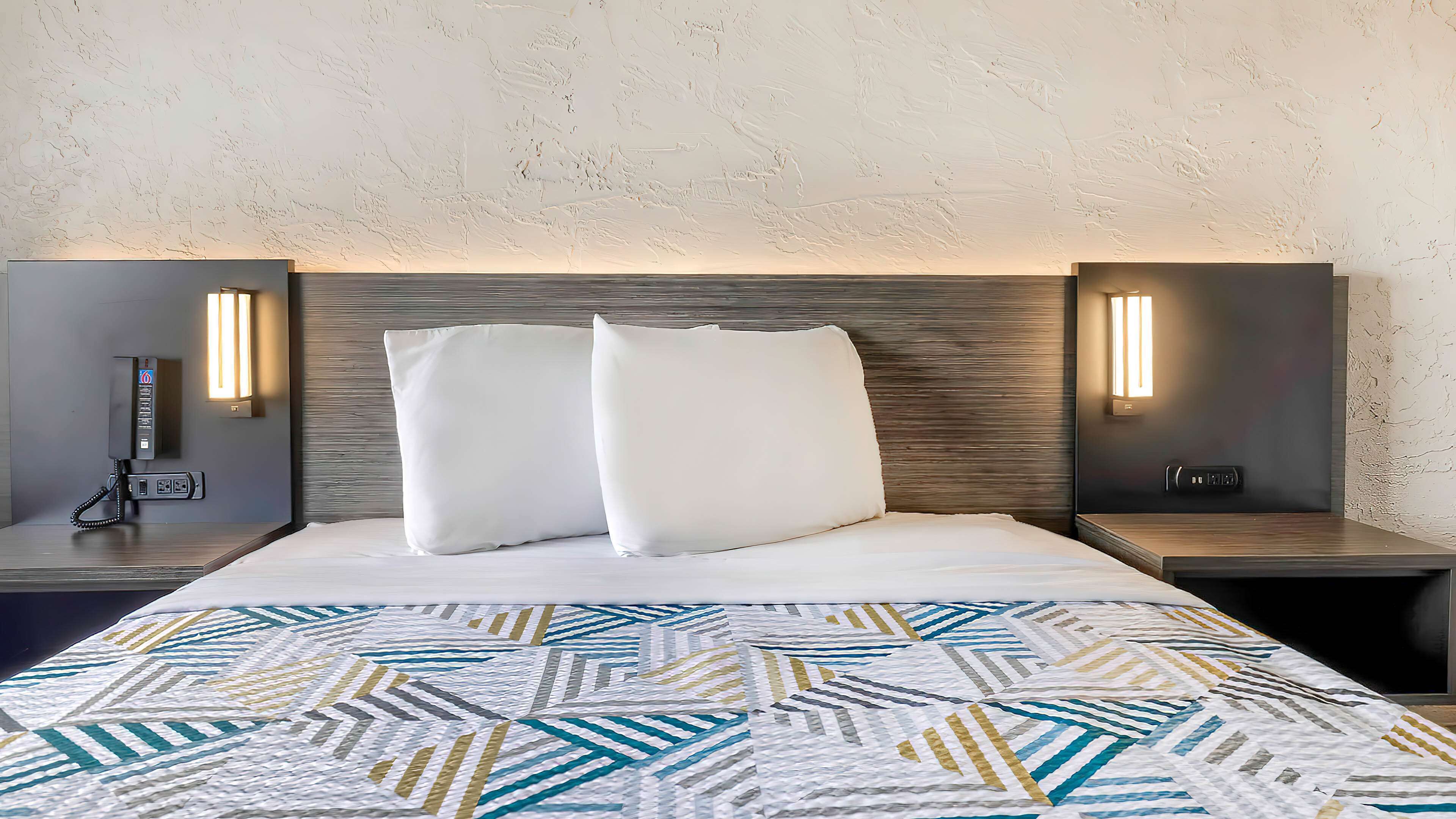 Une chambre d’hôtel avec un grand lit, deux tables de chevet, un téléphone et des lampes fixées au mur.