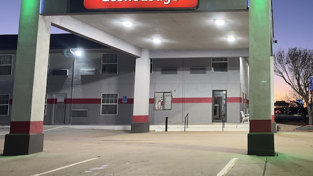 Un letrero de EconoLodge con logotipo rojo y amarillo, un área de estacionamiento y un edificio con múltiples ventanas y una puerta.