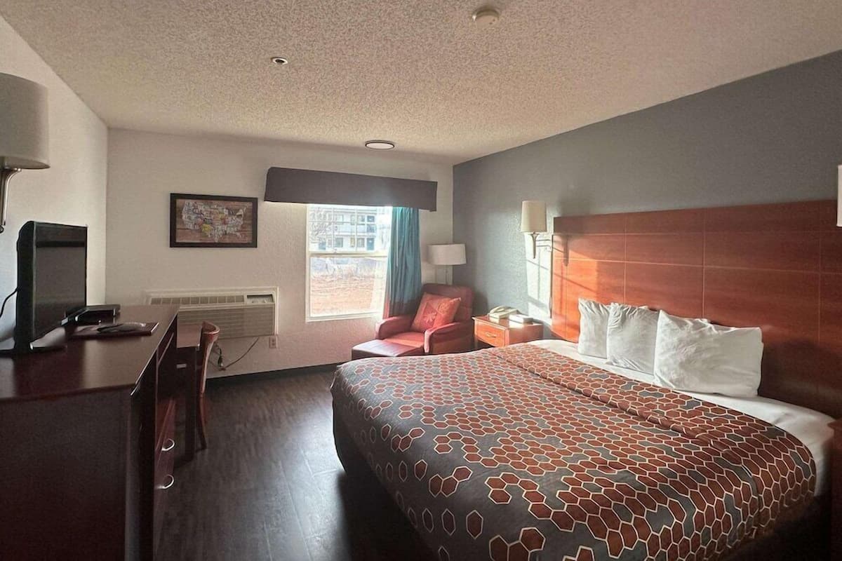 A hotel room with a bed, a desk, a chair, a TV, and a window.