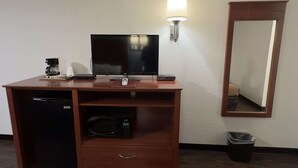 Habitación compacta con escritorio de madera, televisión de pantalla plana, cafetera, microondas y un pequeño cubo de basura.