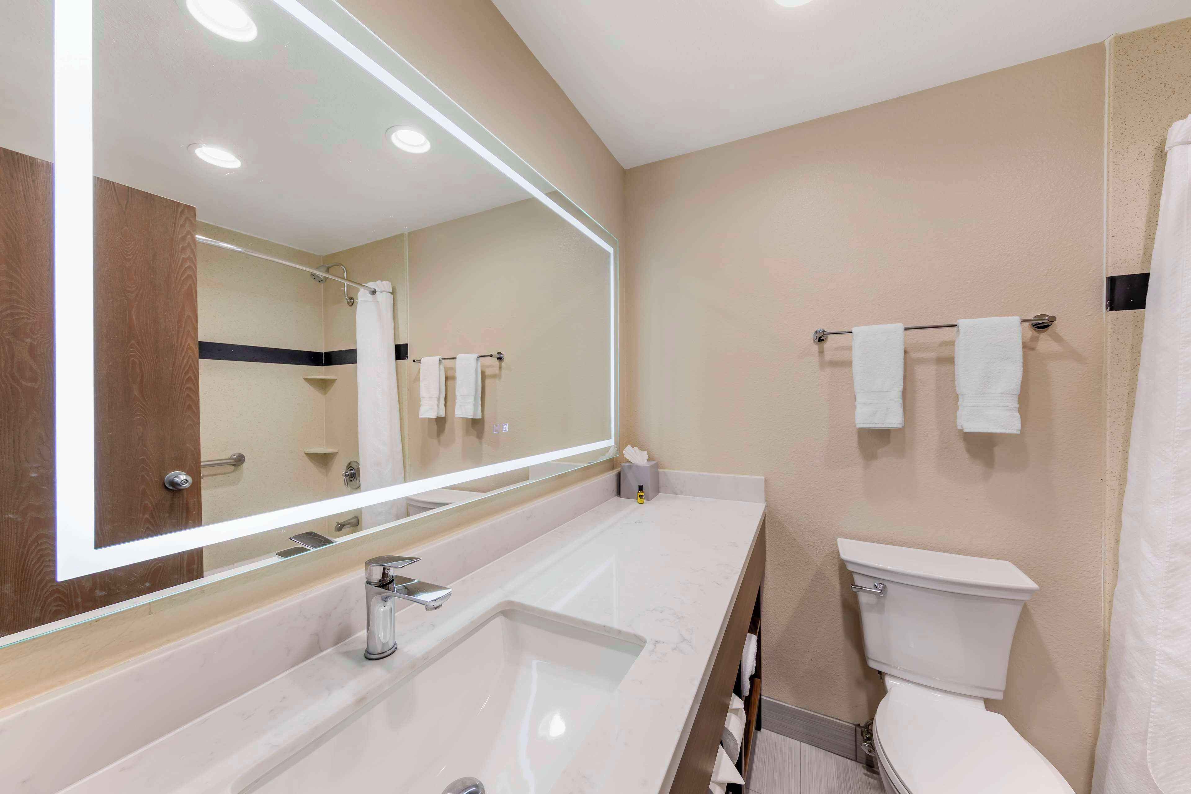 A modern bathroom with a large mirror, a sink, a toilet, and towels on the wall.