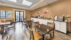 Un área de comedor moderna con mesas y sillas, una encimera de cocina con electrodomésticos, y un amplio ventanal que proporciona luz natural.