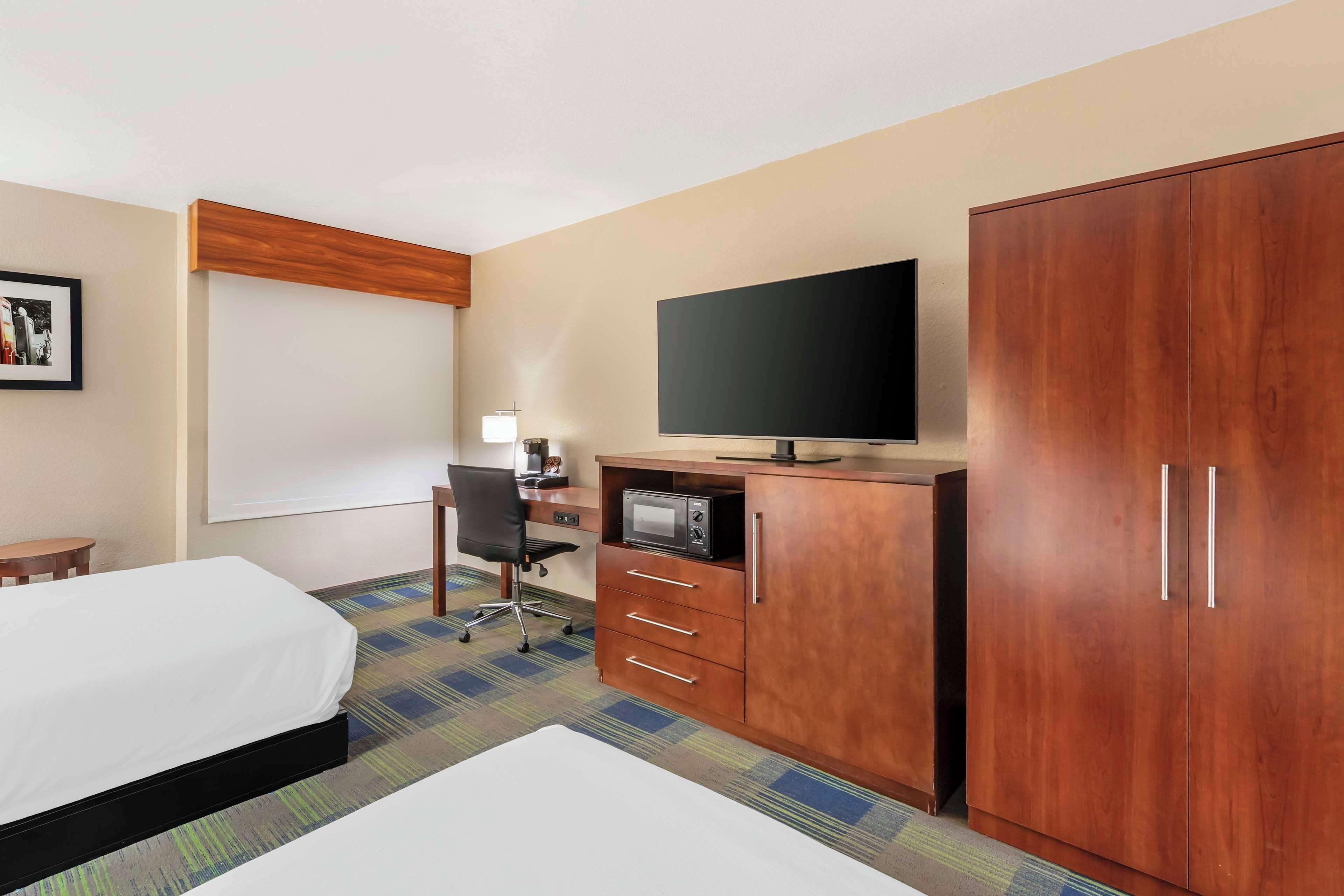 Una habitación de hotel con cama, escritorio, computadora, televisor y armario.