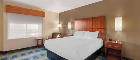 A hotel room with a large bed, bedside tables, a chair, and a window with blinds.