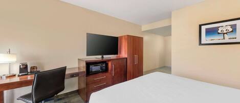 A hotel room with a bed, a desk with a television, a microwave, and a coffee maker.