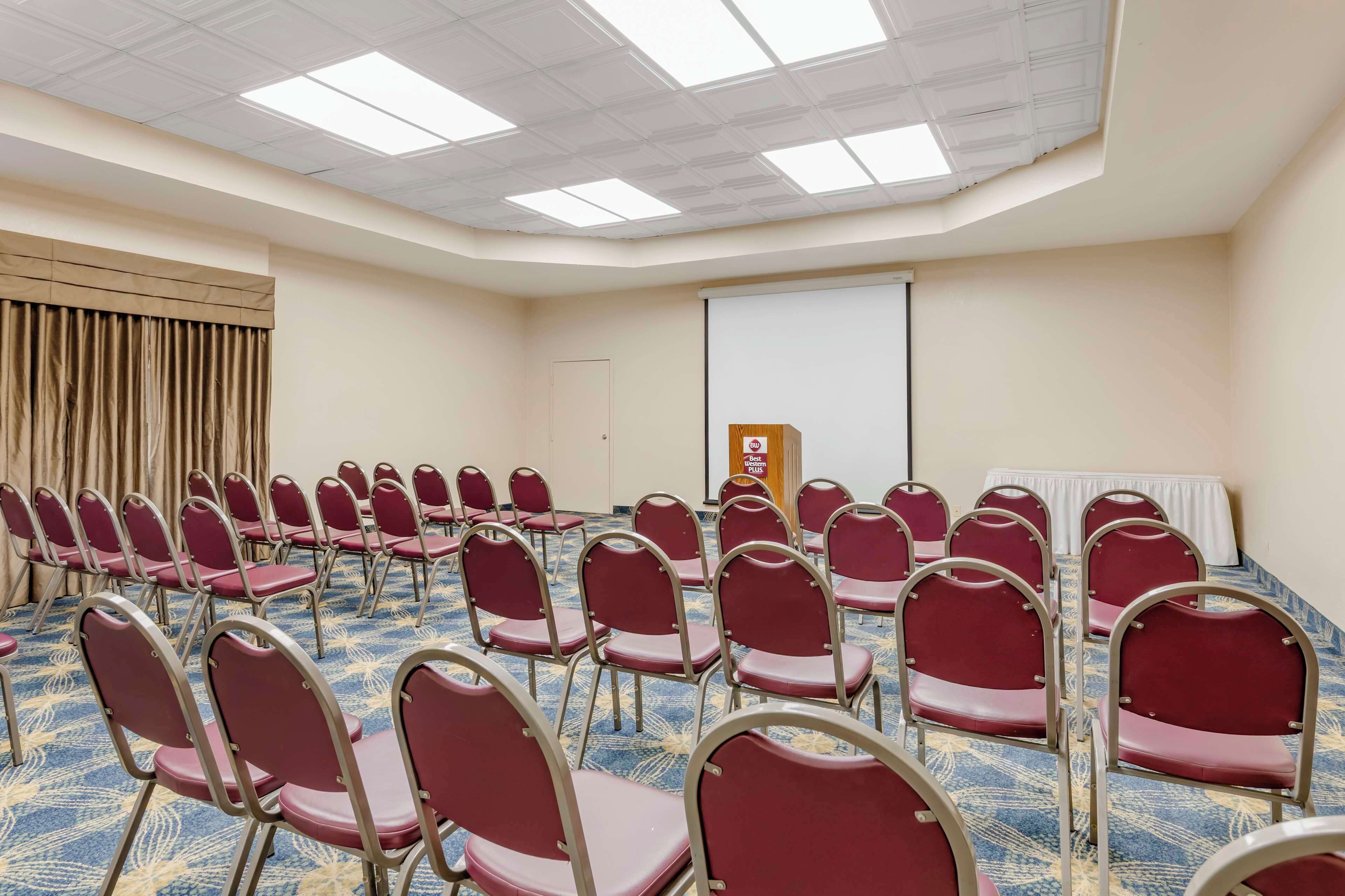 A conference room with rows of red chairs, a projector screen, and a podium.
