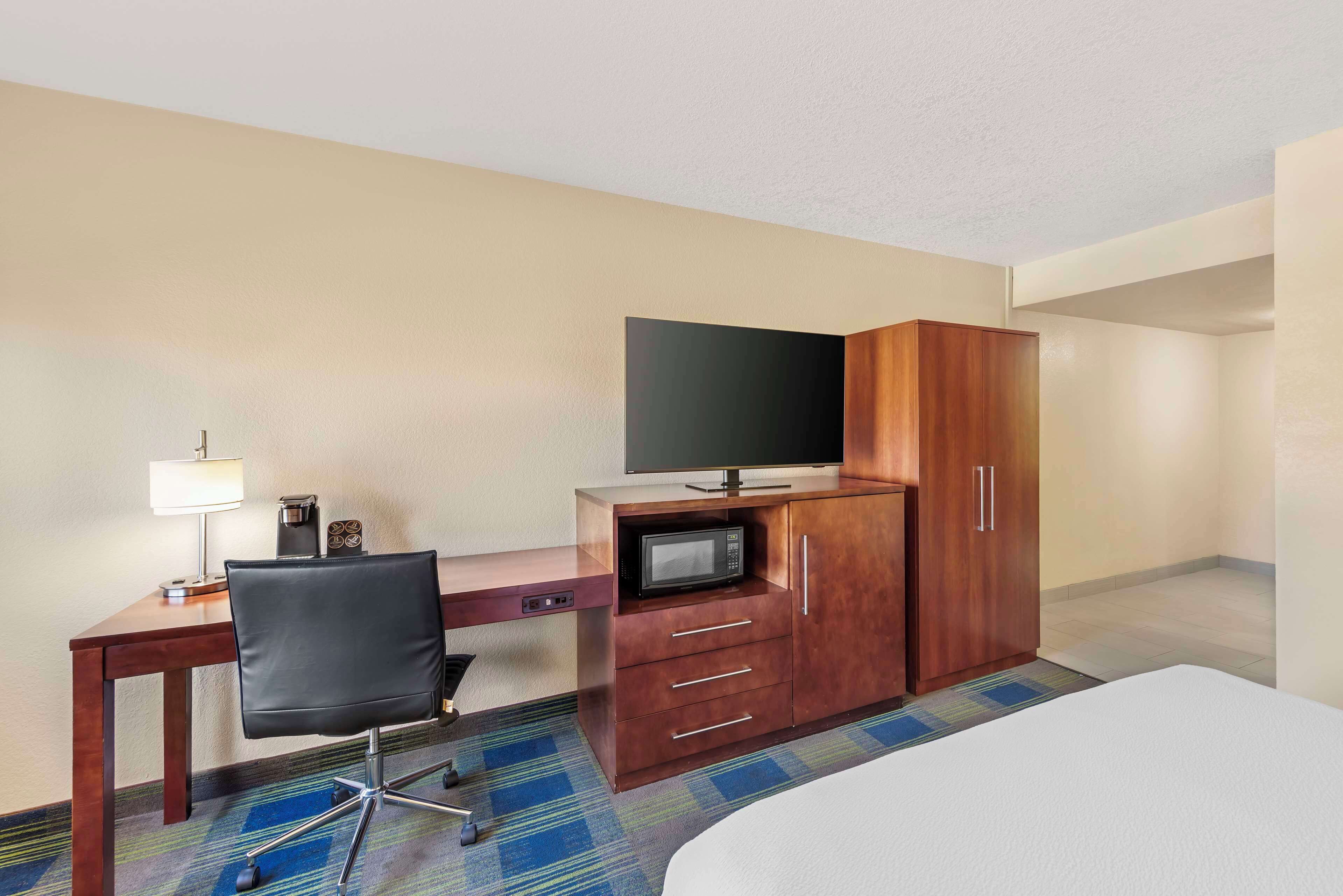 A hotel room with a bed, a desk with a chair, a television, a microwave, and a wardrobe.