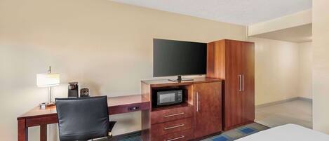 A hotel room with a bed, a desk with a chair, a television, a microwave, and a wardrobe.