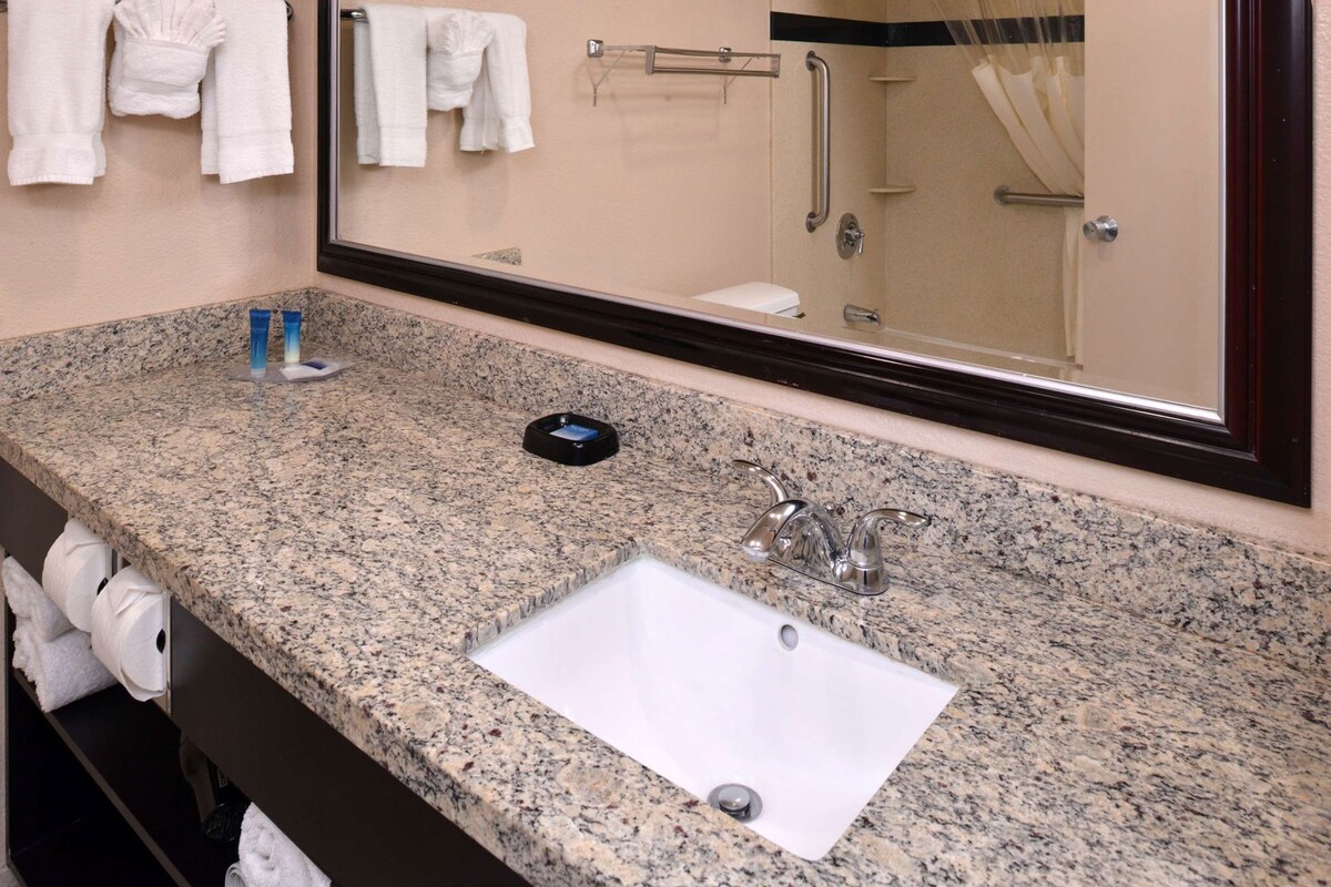 A bathroom with a granite countertop, a white sink, a mirror, and a towel rack.