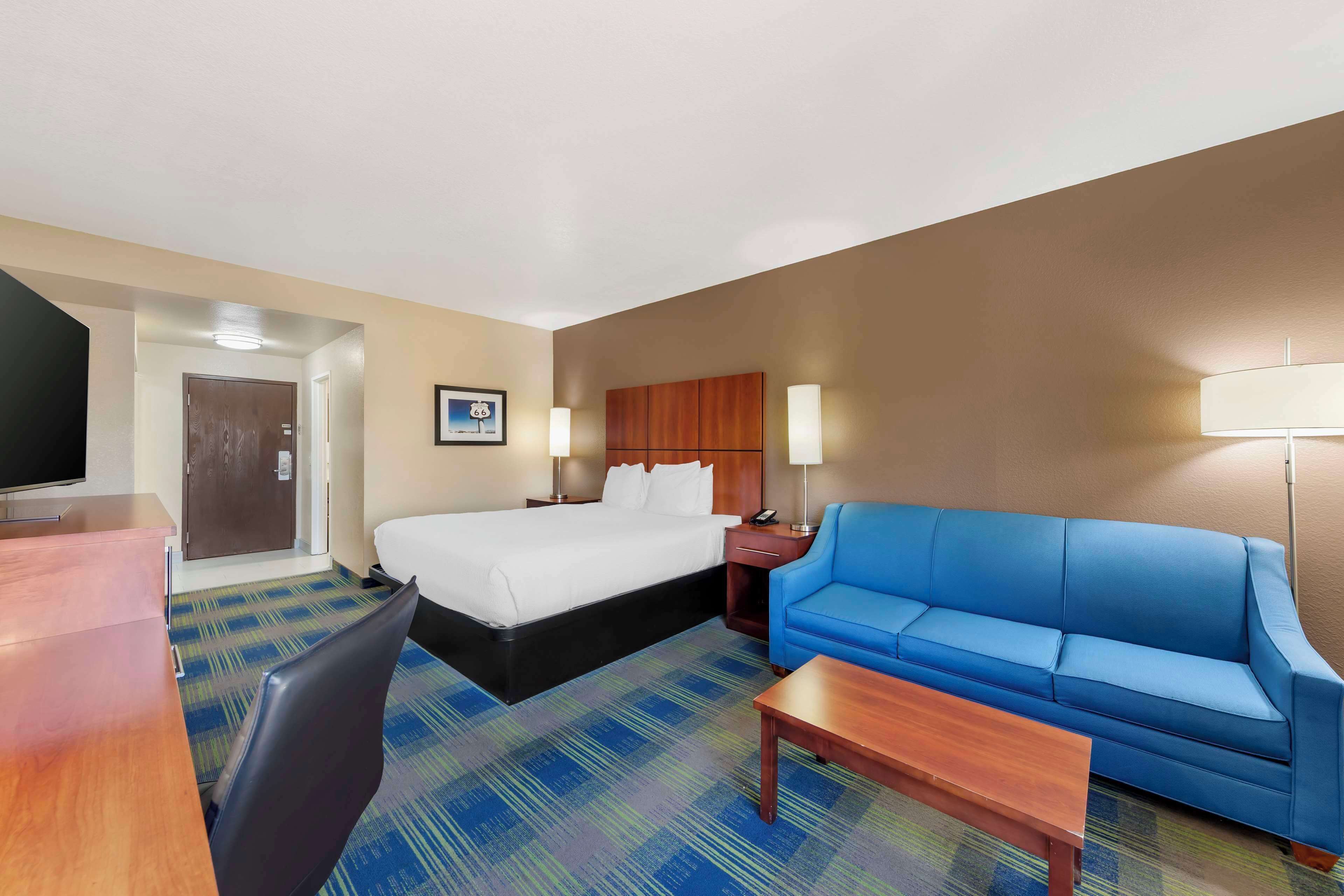 A hotel room with a bed, a blue sofa, a desk, and a television.
