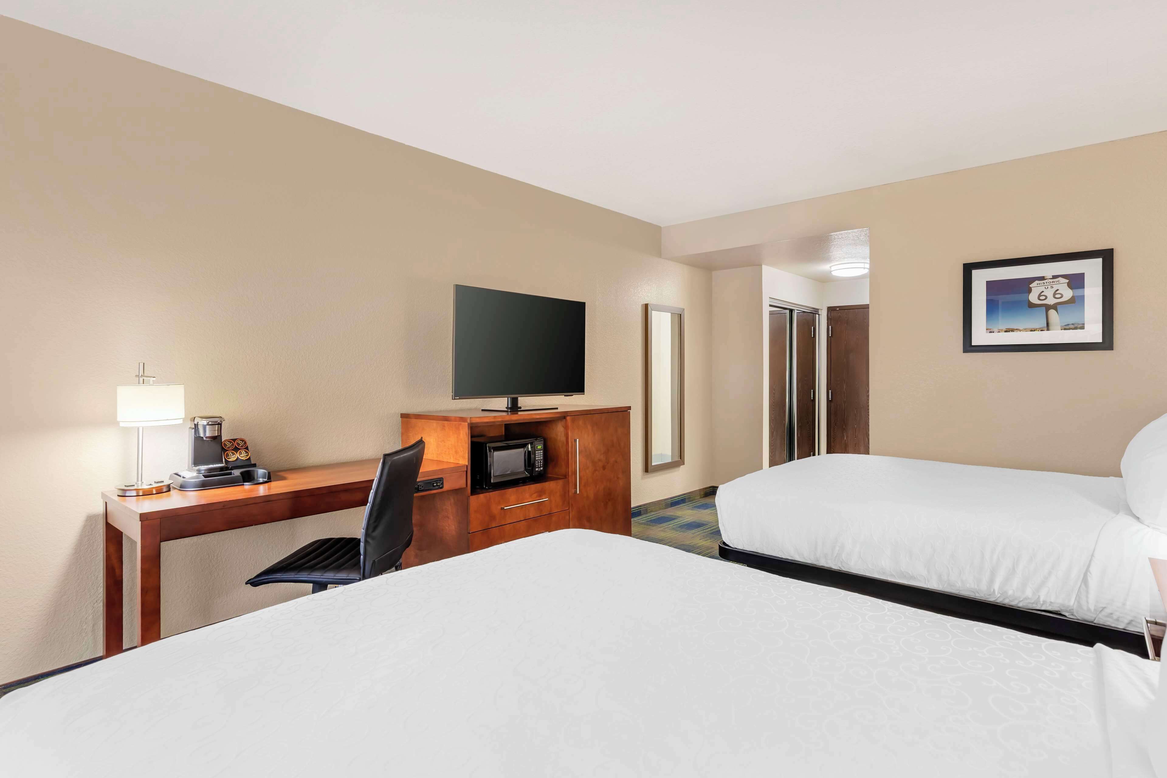 A hotel room with two beds, a desk with a TV, a coffee maker, and a framed picture of Route 66 on the wall.