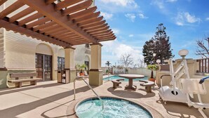 Un área de piscina con jacuzzi, mobiliario exterior y una pérgola.