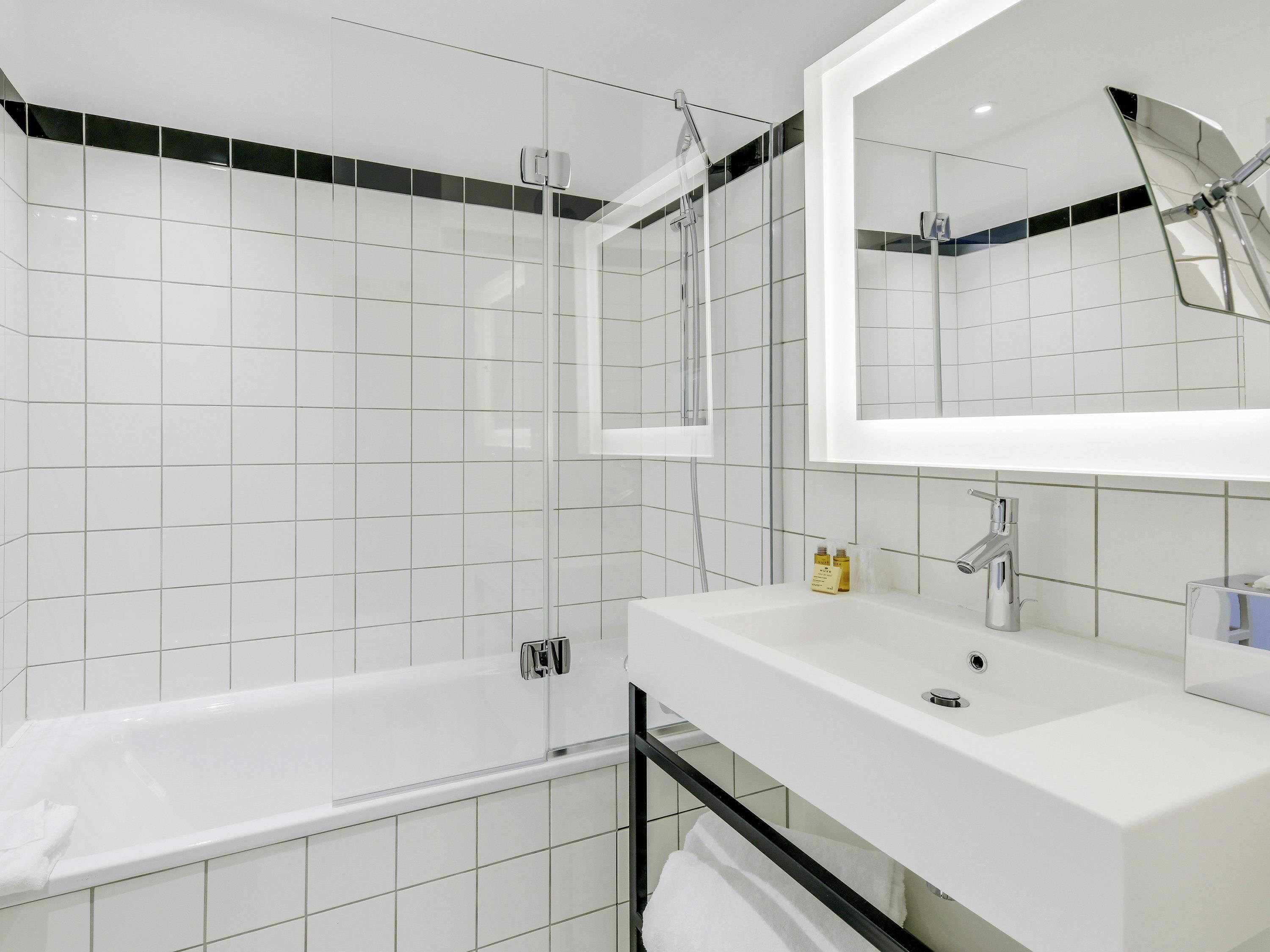 Un baño moderno con ducha de vidrio, lavabo blanco y un espejo grande.