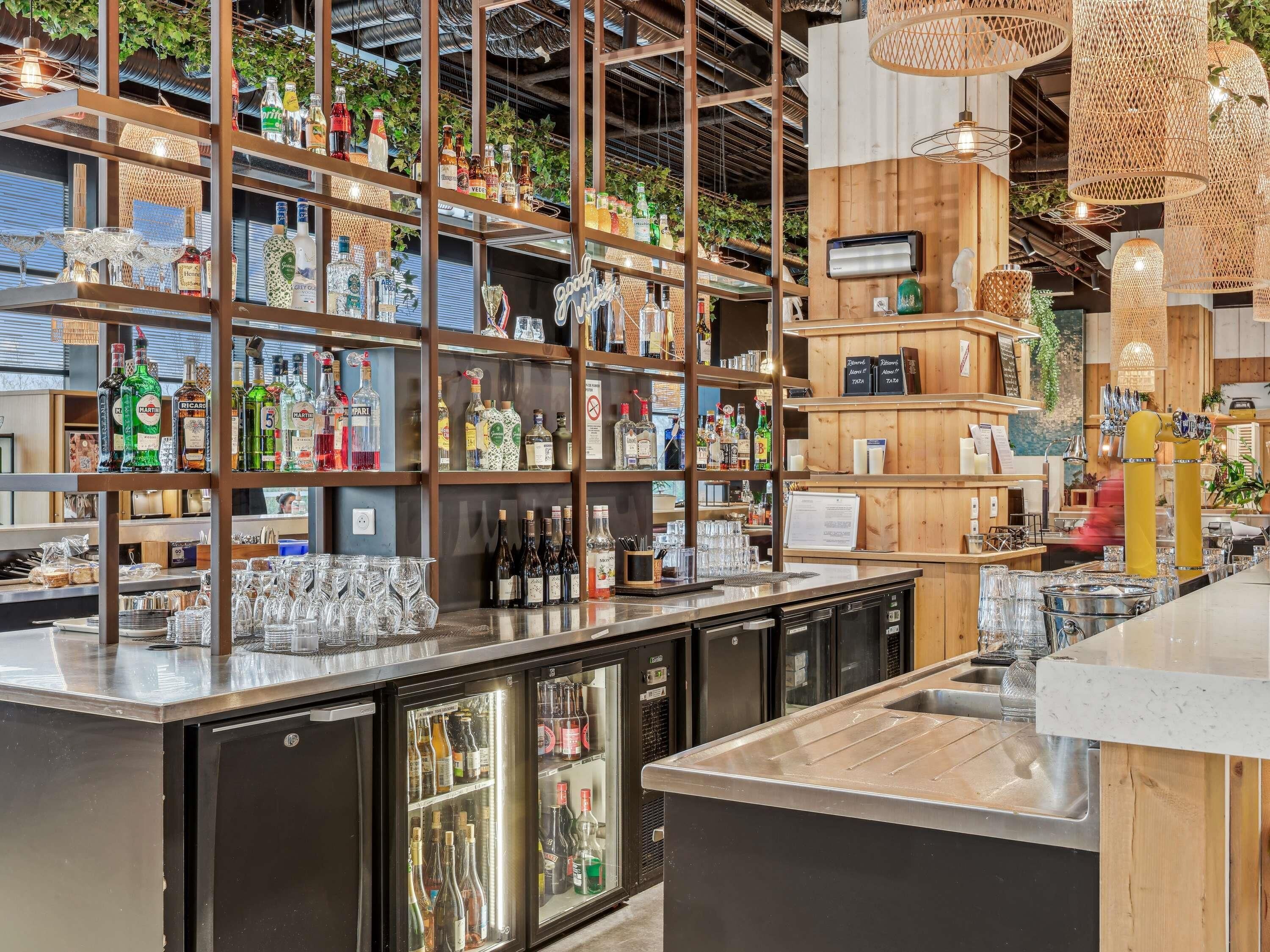 Uma área de bar com prateleiras de garrafas de bebidas, copos e um refrigerador.