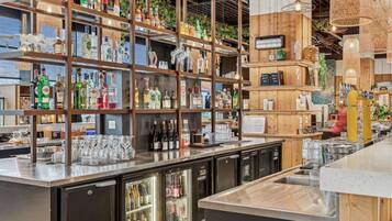 Uma área de bar com prateleiras de garrafas de bebidas, copos e um refrigerador.