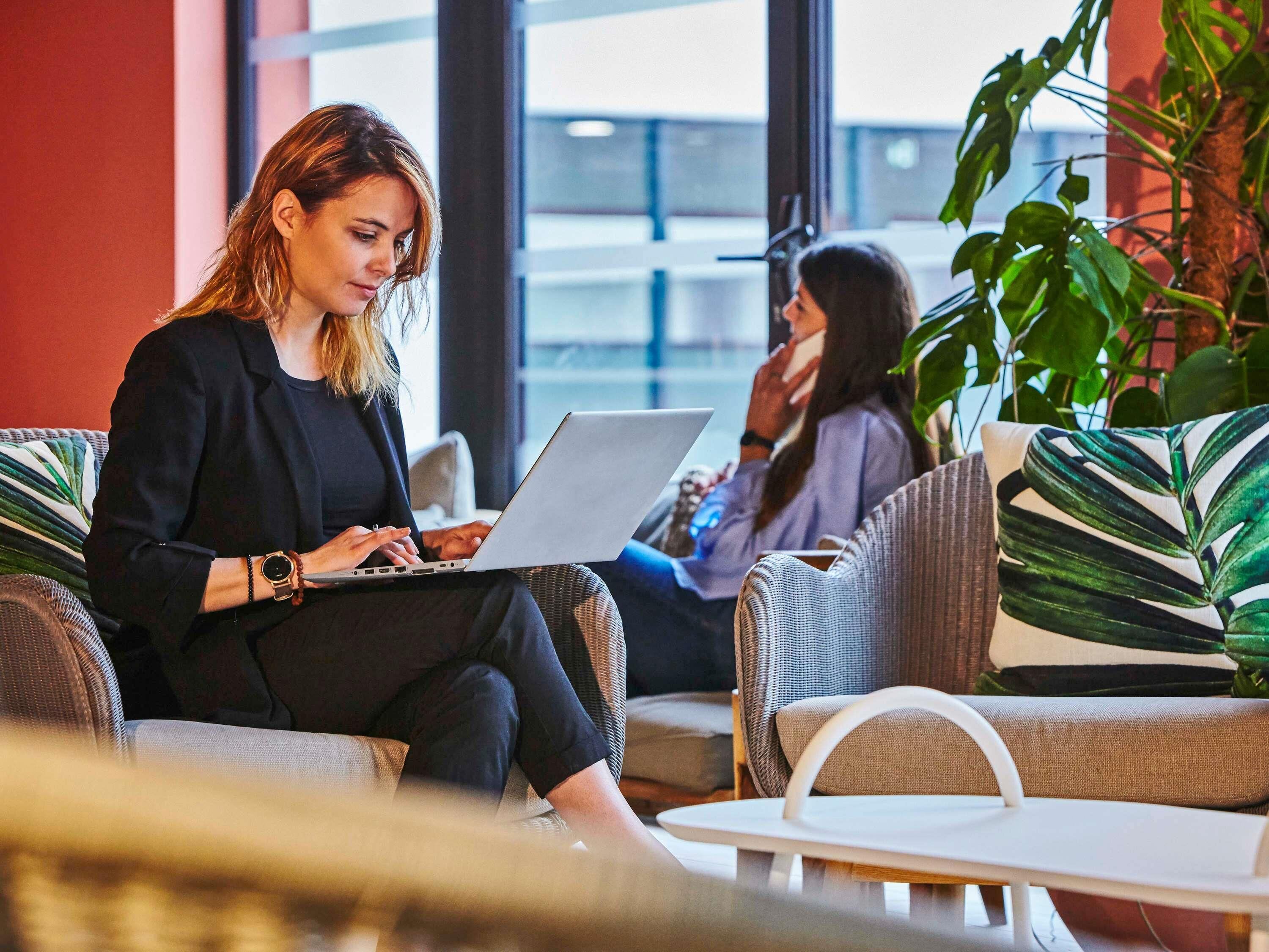 A person using a laptop in a modern indoor setting with comfortable seating and large windows.