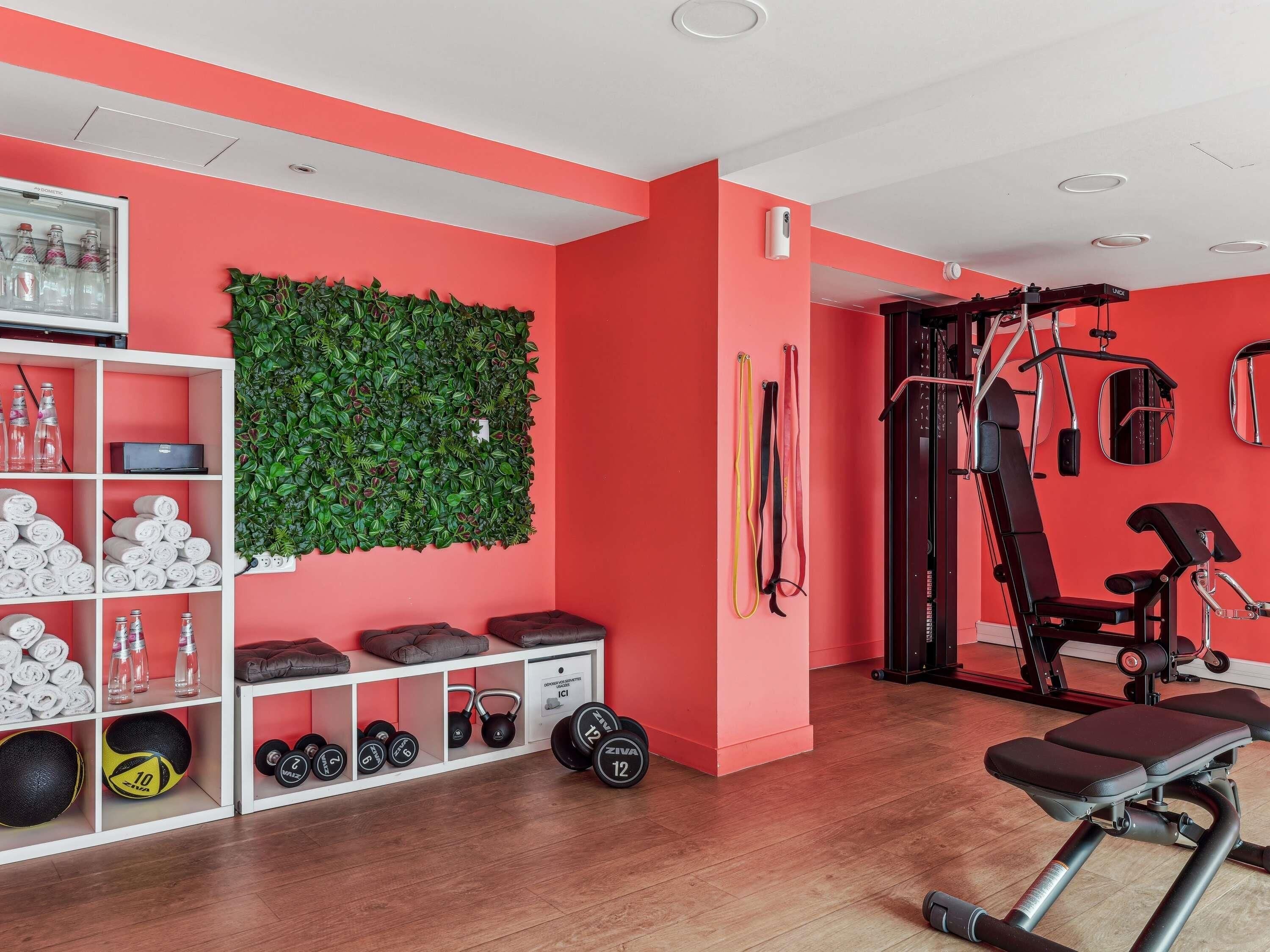 A gym with a red wall, a green wall-mounted plant, and various exercise equipment.