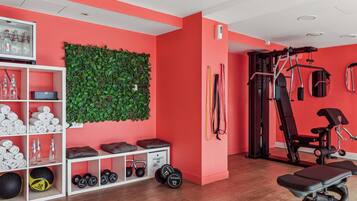Un gimnasio con una pared roja, una planta verde montada en la pared y varios equipos de ejercicio.