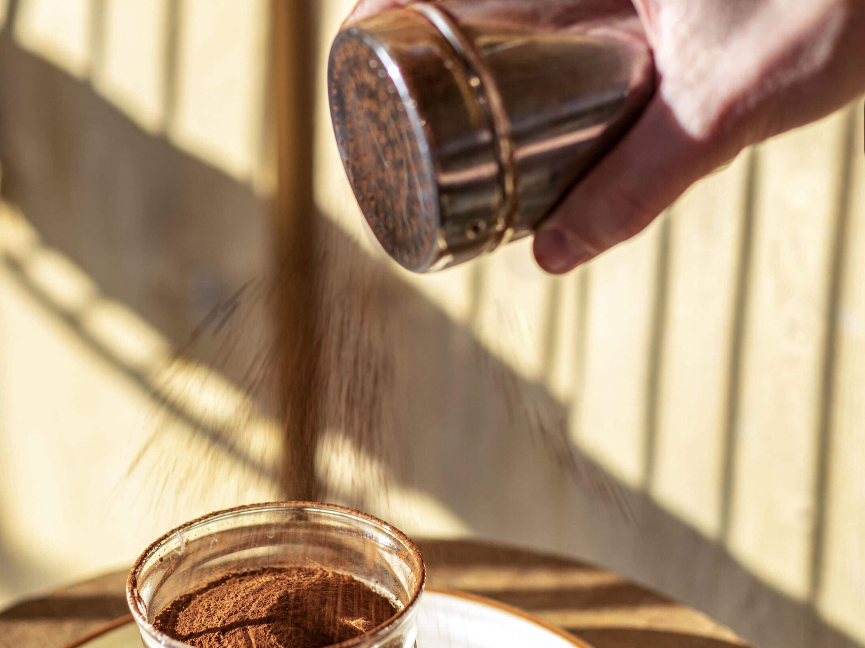 A hand pouring a powdery substance into a clear glass.