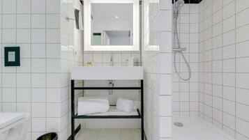 A modern bathroom with a white tiled wall, a white sink with a mirror above it, a black metal shelf with towels, and a shower area.