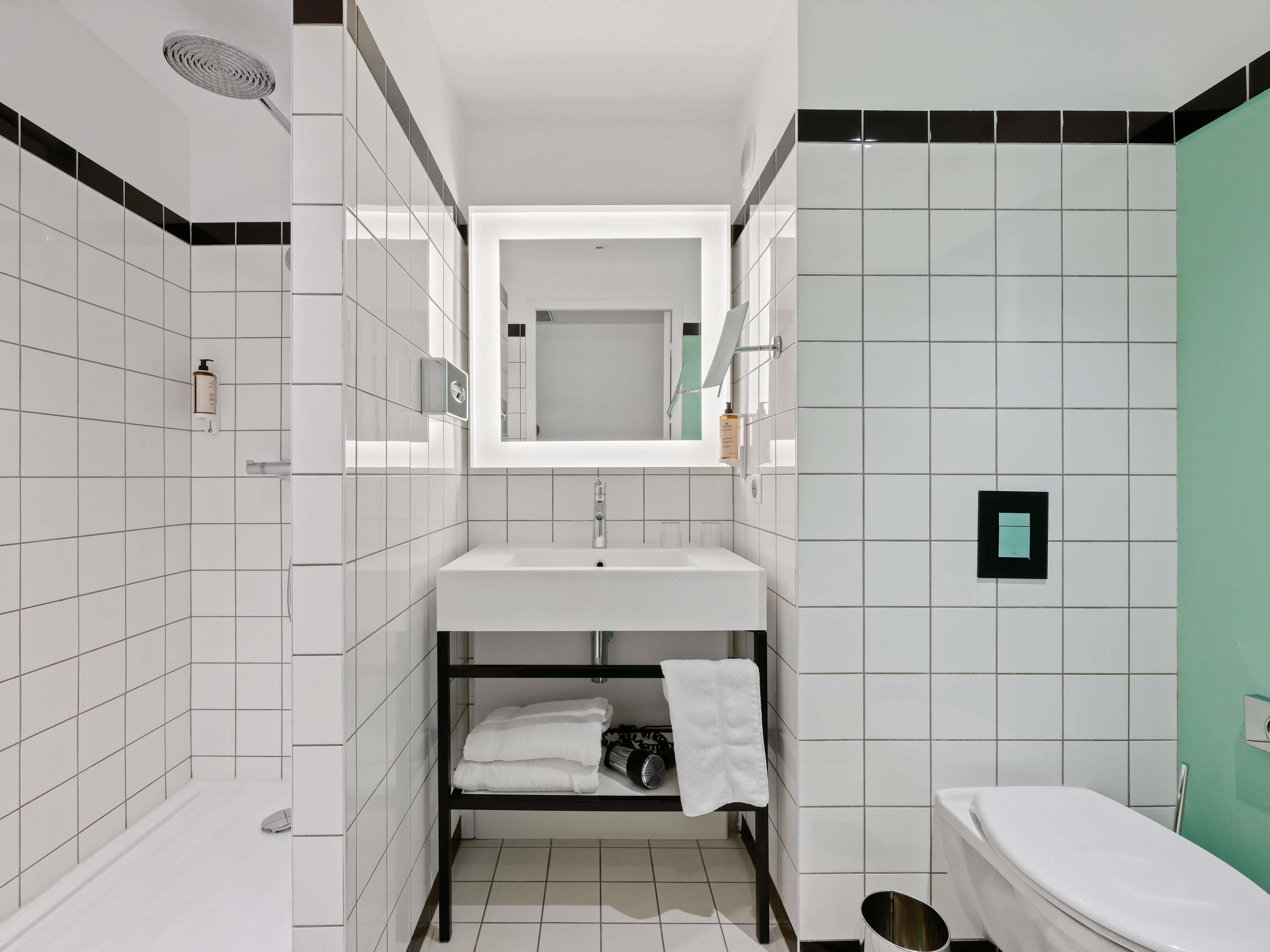 Un bagno compatto con lavandino bianco, specchio, doccia e WC.