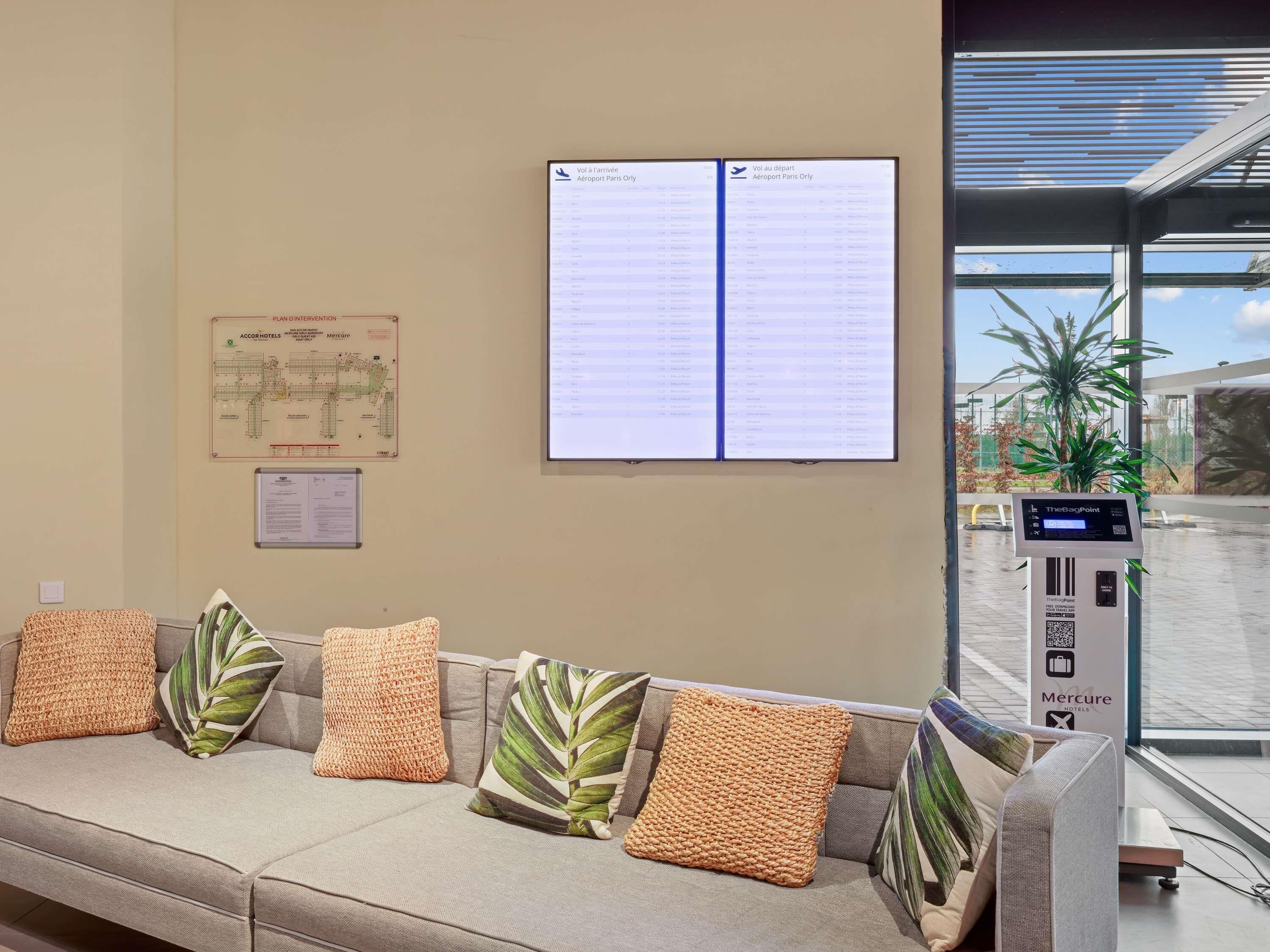 Zona de recepción con área de descanso, un panel informativo digital, un quiosco de autoservicio TheBagPoint y un mapa del hotel.