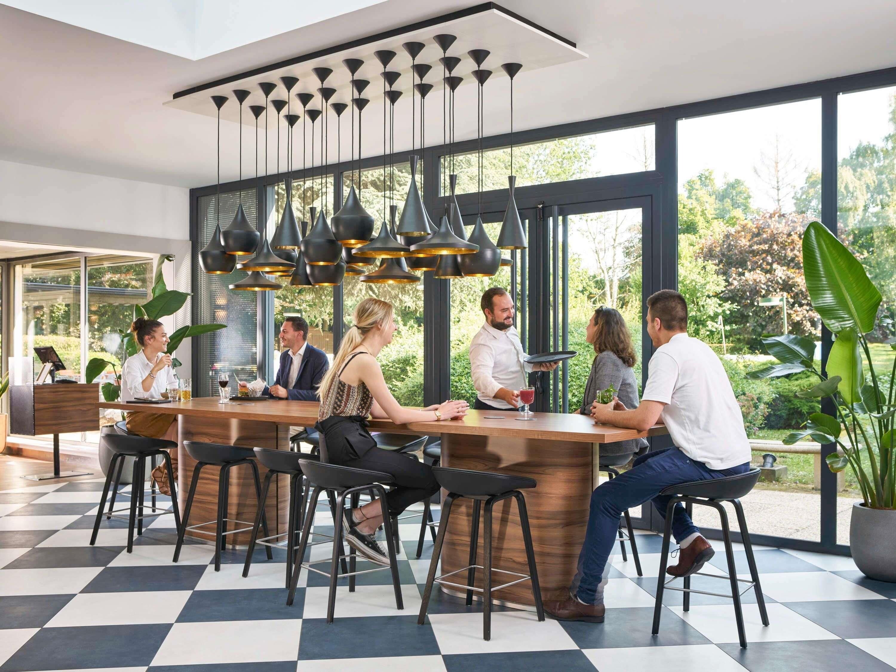 A modern bar area with a checkered floor, black bar stools, and pendant lighting.
