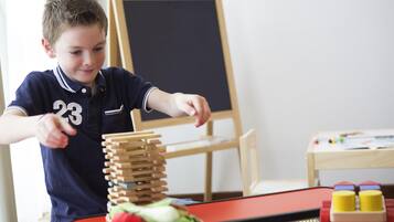 A child playing with wooden blocks and a basket of vegetables on a table.