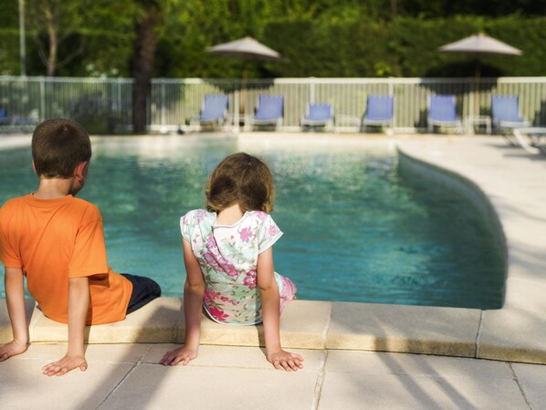 Two individuals sitting by a poolside, with lounge chairs and umbrellas in the background. - Novotel Massy Palaiseau (Palaiseau)