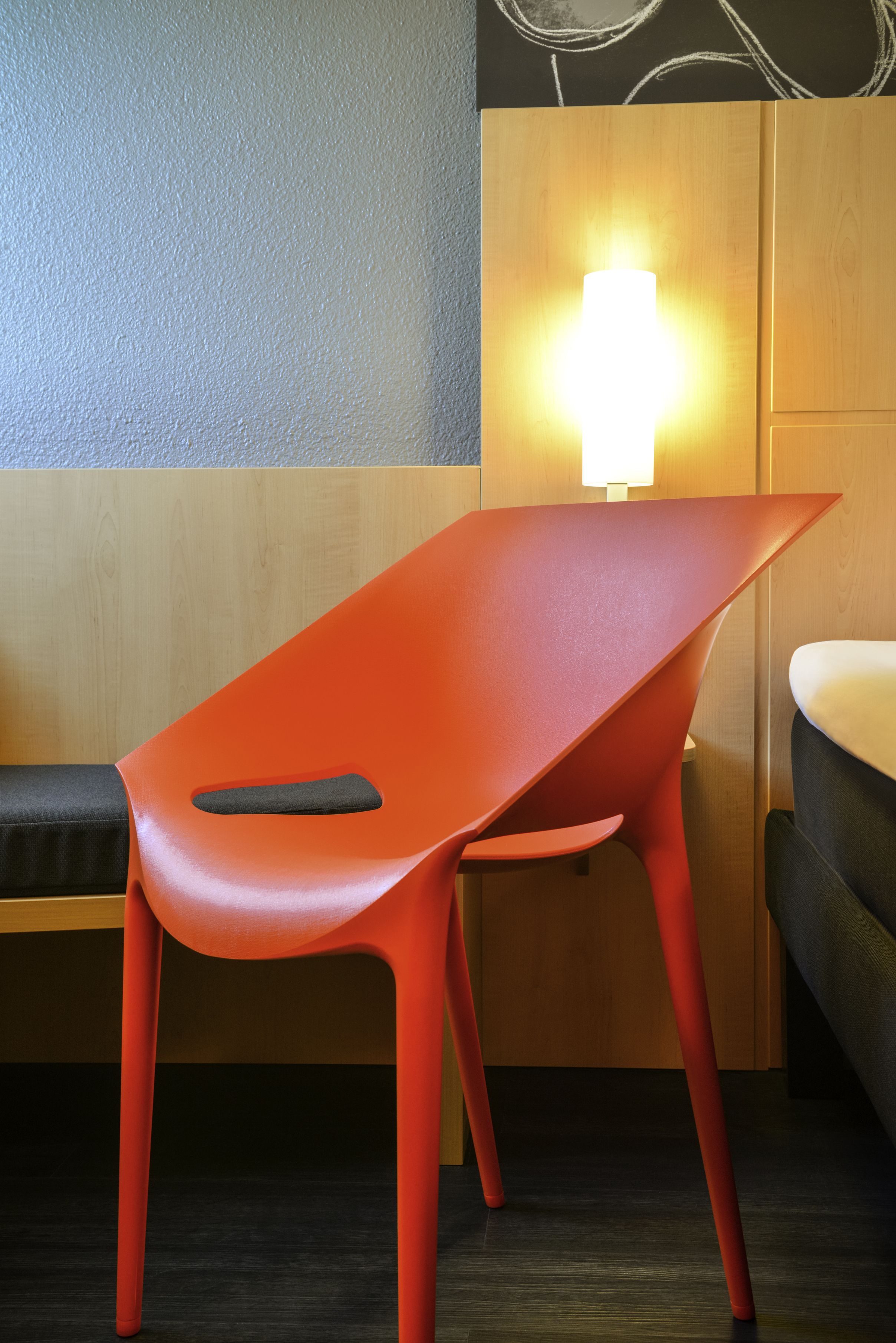 Una habitación moderna con cabecera de madera, una silla roja y una cama con cabecera blanca.