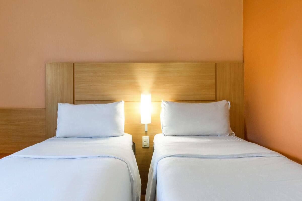 A double room with two beds, a wooden headboard, a night light, and a wall switch.