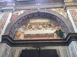 A detailed fresco of the Last Supper above a doorway with inscriptions.