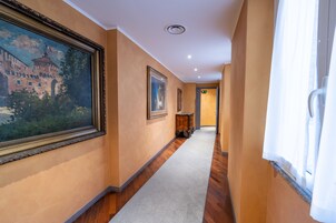 Ένας διάδρομος με έναν μεγάλο πίνακα σε κορνίζα, μια ξύλινη ντουλάπα και μια πόρτα με μια επιγραφή.