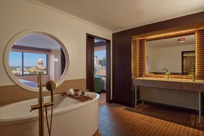A modern bathroom with a bathtub, a round mirror, and a view of a cityscape.