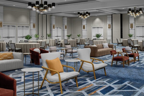 A hotel lobby with round tables, chairs, sofas, and a patterned carpet.