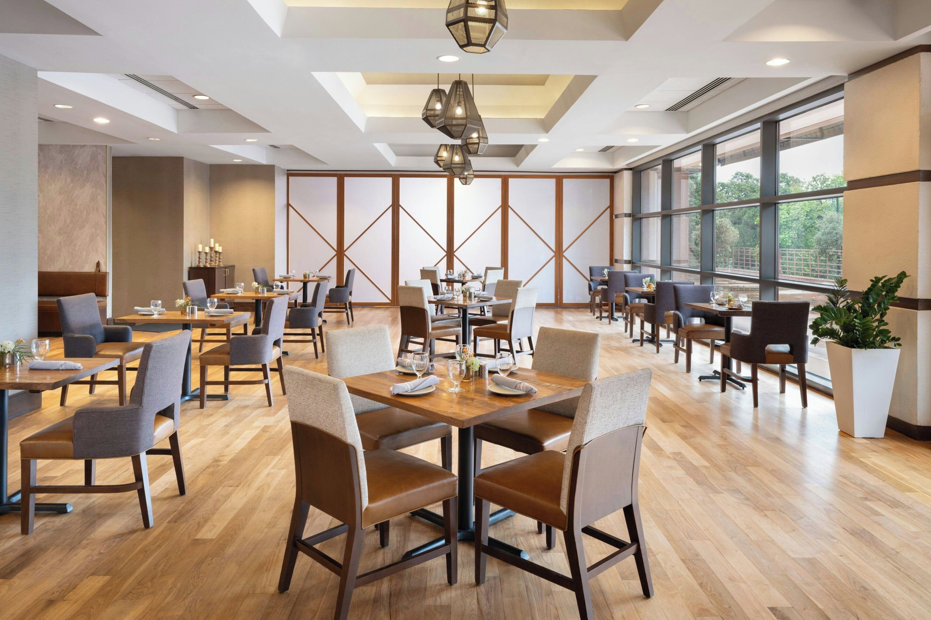 Un vaste espace dédié à la salle à manger, avec de nombreuses tables et chaises, de grandes fenêtres et un design moderne au niveau du plafond.