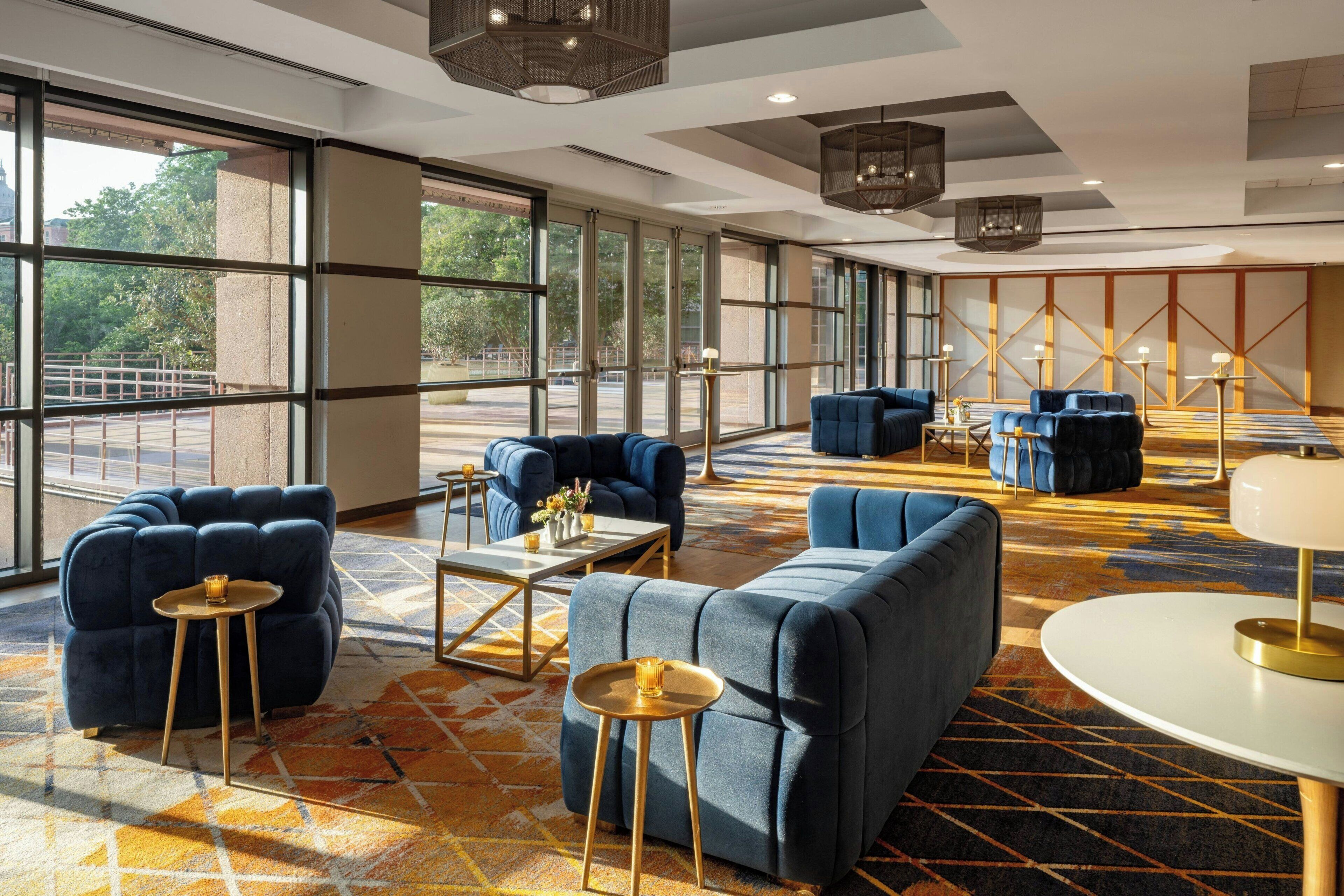 A spacious lobby with large windows, blue upholstered seating, and a patterned carpet.