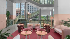 A modern indoor space with a central staircase, multiple seating areas with round tables, and large windows offering views of the surrounding buildings. - Renaissance Austin Downtown Hotel (Austin)