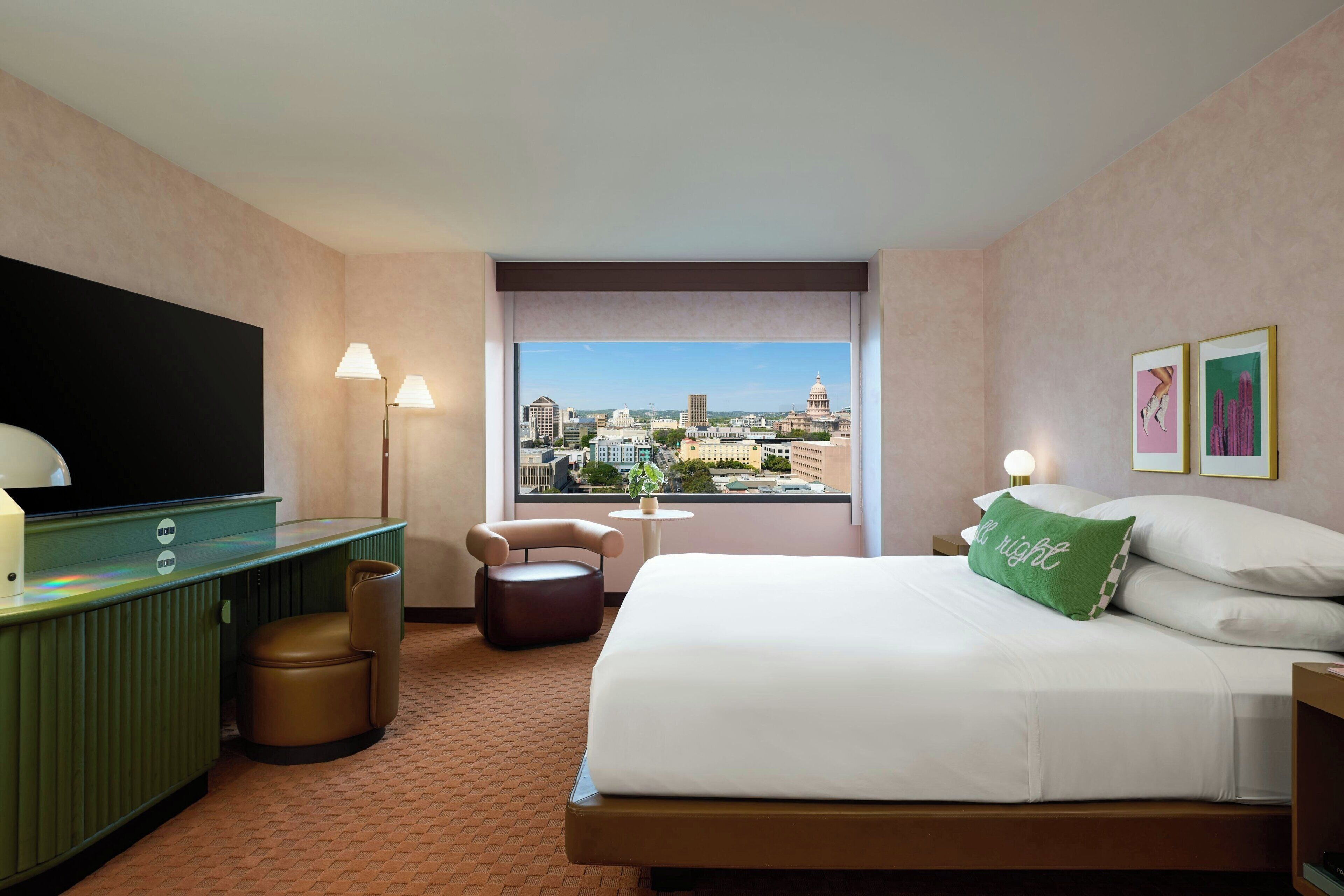 Habitación de hotel con cama, escritorio, silla, televisión, ventana con vista a la ciudad y una mesita.