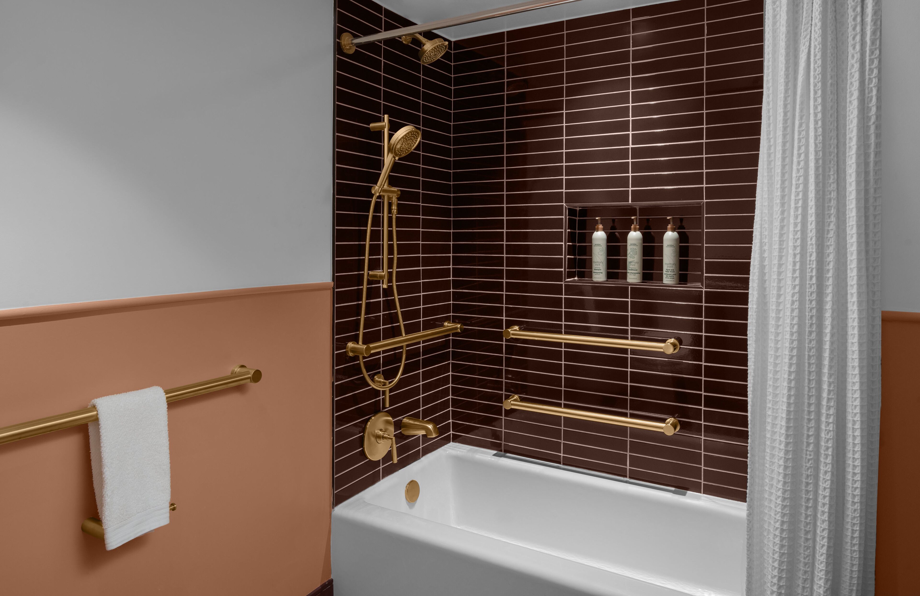 A bathroom with a bathtub, a shower with a golden showerhead, and a towel rack with a white towel.