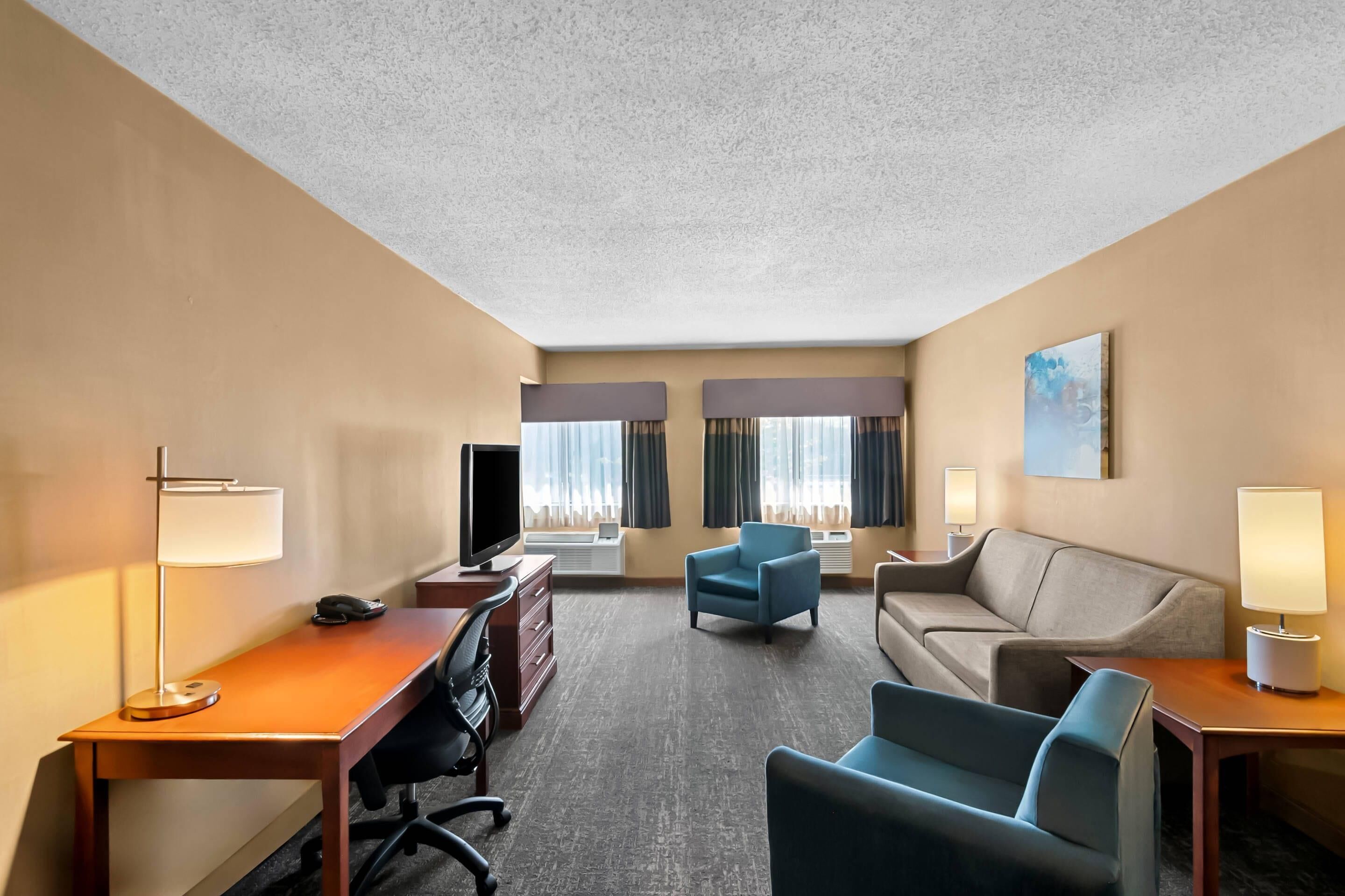 Quarto de hotel com escrivaninha, duas poltronas, um sofá, uma televisão e um quadro na parede.