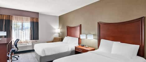 A hotel room with two beds, a desk, a chair, a lamp, and a window with curtains.