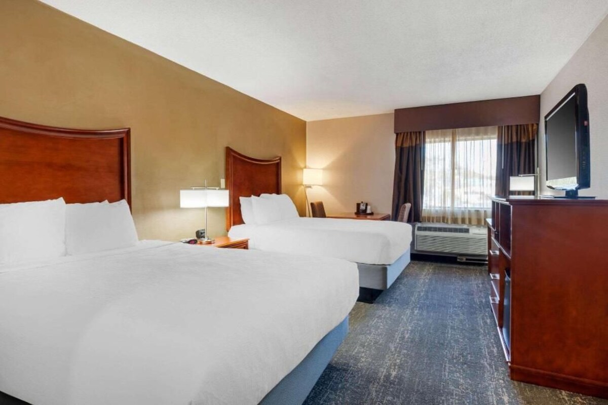 A hotel room with two beds, a desk, a TV, and a window with curtains.