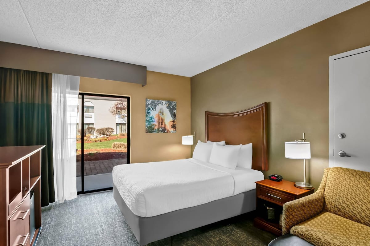 Une chambre d’hôtel avec un lit, un bureau, une chaise, une lampe et un tableau au mur.