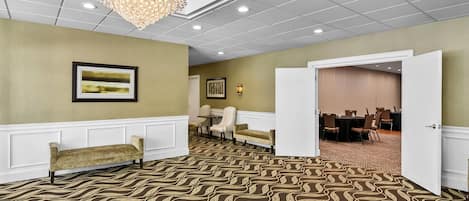 A hotel lobby with a patterned carpet, a chandelier, framed artwork, and a view into a dining area.